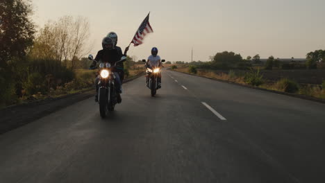 siluetas de ciclistas viajan por la carretera al atardecer con la bandera estadounidense