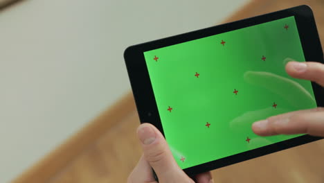 manos masculinas sosteniendo una tableta con pantalla verde. hombre haciendo gestos en la pantalla de la tableta