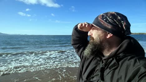 Active-bearded-male-looking-out-across-windy-island-seascape-ocean-waves-at-sunrise