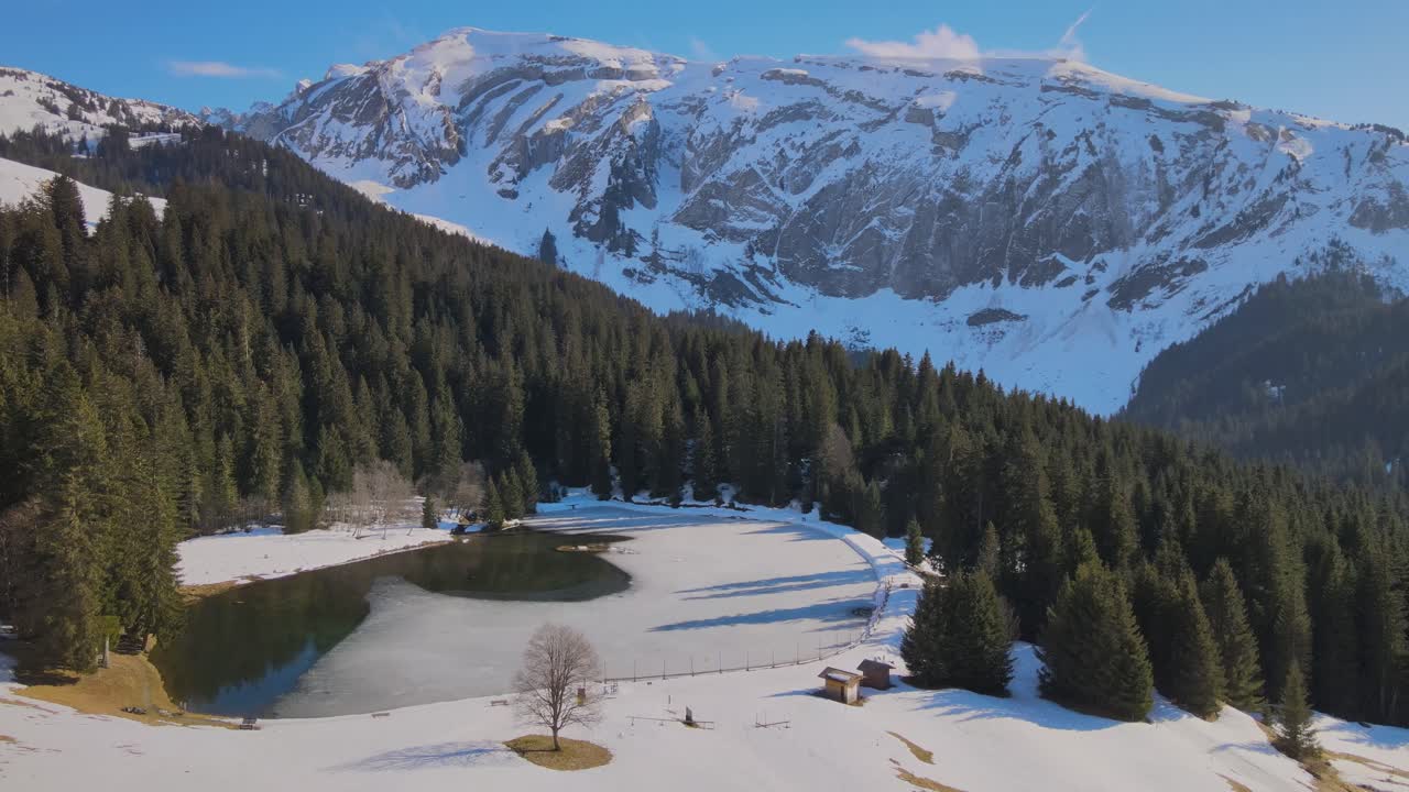 pequeño lago artificial en la zona montañosa francesa con bosque y acantilados nevados en el fondo