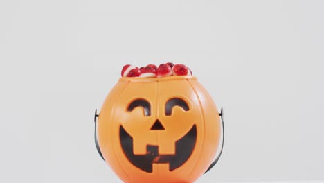 Scary-halloween-pumpkin-printed-bucket-full-of-candies-against-grey-background