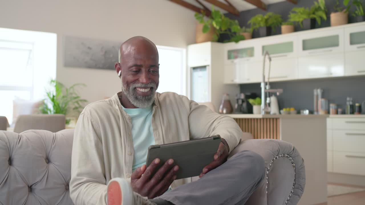 Mature African American man responding to tablet prompt, tapping, adjusting angle, smiling on couch