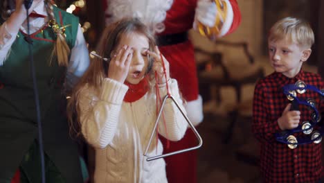 beautiful little girl singing and dancing with santa and elf. happy children spend great time at christmas indoors. close-up.