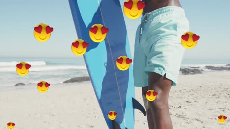 Multiple-heart-eyes-emojis-floating-against-african-american-man-with-surfboard-on-the-beach