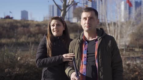 su esposa le está diciendo algo al hombre con discapacidad visual en el parque.