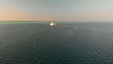 Flying-towards-boat-during-golden-hour-sunset-over-the-Arabian-Gulf,-Arial-view