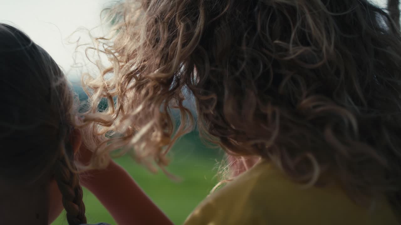 Close up of woman's hair in the wind holding daughter on the knee and swinging in summer day.