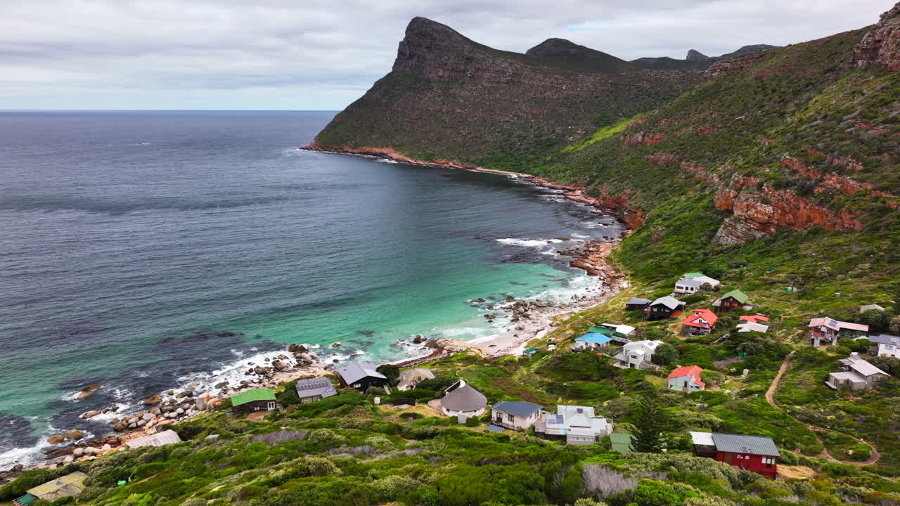 South Africa small beach town Smitswinkel Bay Cape of Good Hope Simon's Town aerial drone cinematic homes surf wave green lush spring summer deep aqua blue ocean cloudy mountain still tripod