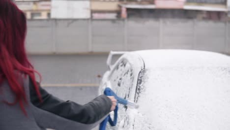 young woman in coat applying foam on her silver sportcar with special jet on self-service carwash