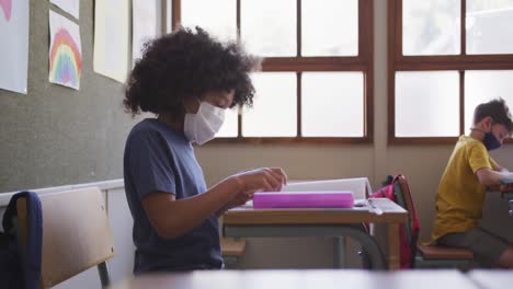 Junge-Mit-Gesichtsmaske-Niest,-Während-Er-In-Der-Schule-Auf-Seinem-Schreibtisch-Sitzt