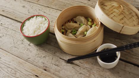 composition of bamboo steamer with gyoza dumplings and soy sauce on wooden background