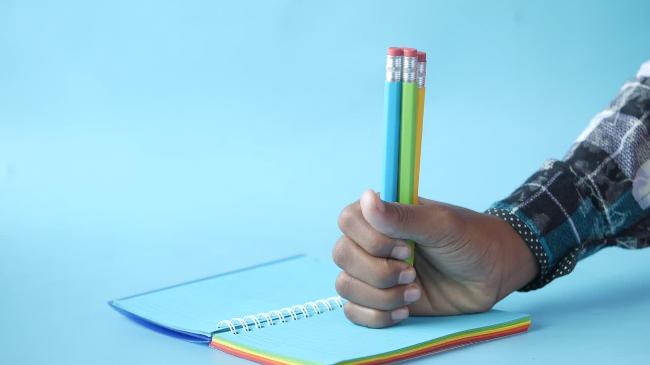mano sosteniendo lápices sobre un cuaderno de colores