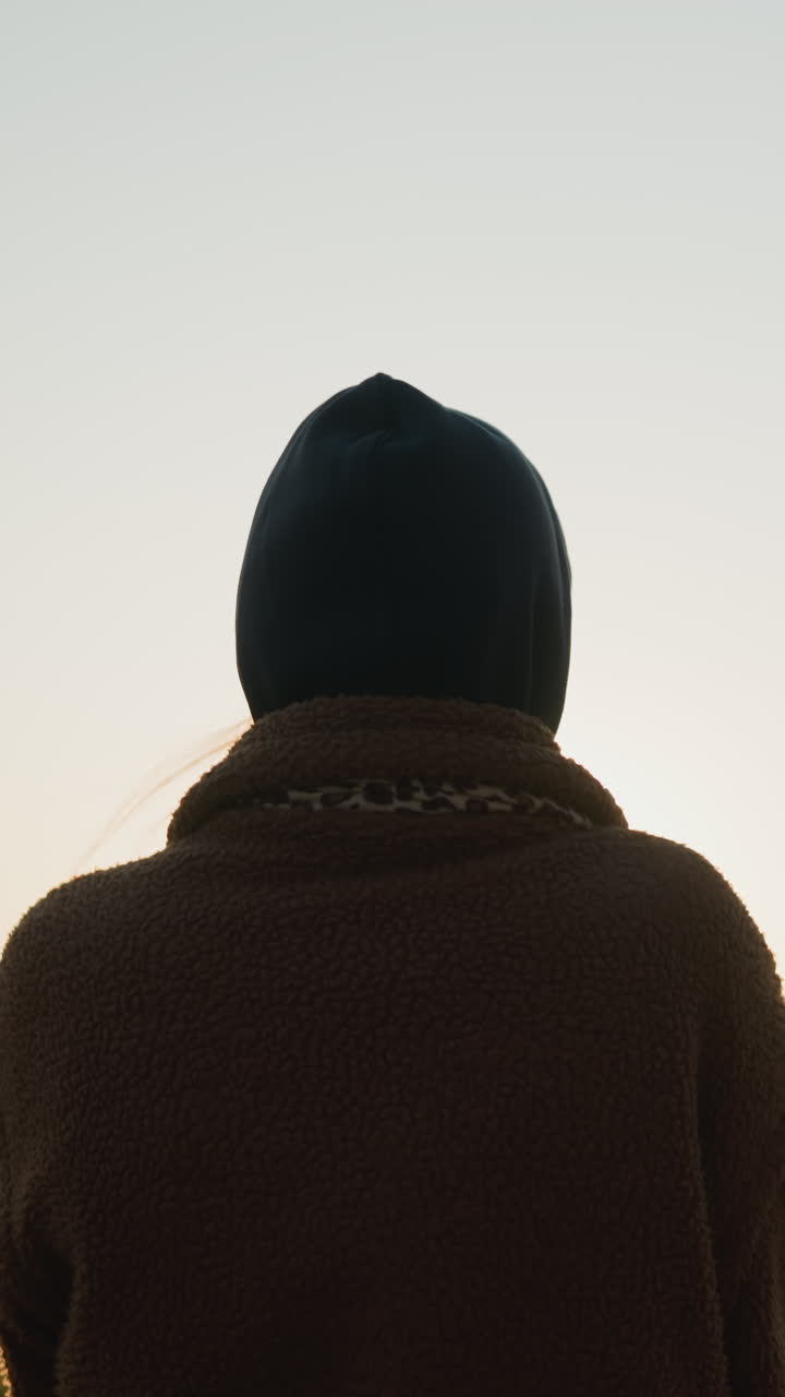 해가 지는 동안 공원을 가로질러 희미하게 고 있는 여자의 뒷면 사진, 가는 태양의 부드러운 황금빛이 그녀의 실루을 둘러싸고 따뜻한 빛을 발한다.