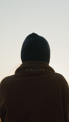 back shot of a woman walking faintly through a park at sunset, with the soft golden light of the setting sun casting a warm glow around her silhouette. the background is blurred