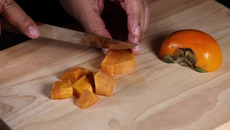 hands slicing persimmon into cubes on board