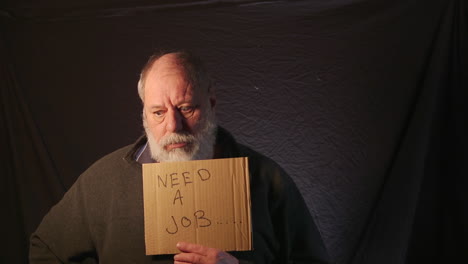 old homeless unemployed man holding a need a job card