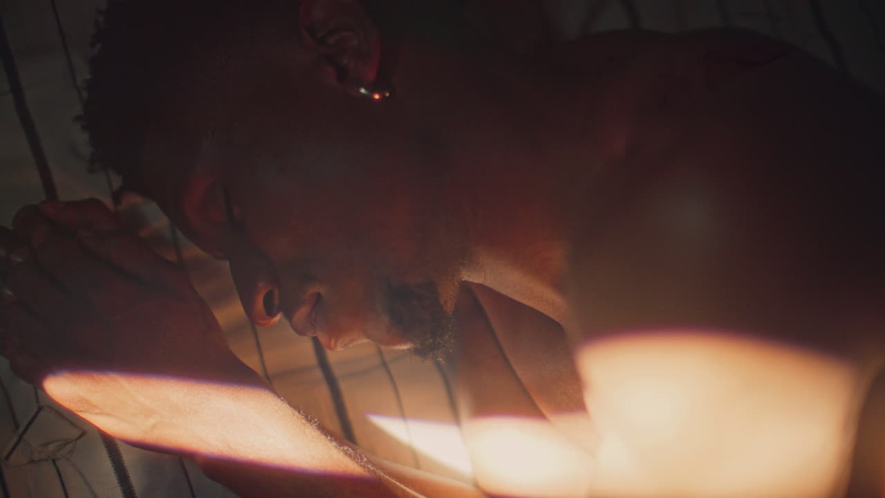 Young African American Man Sleeping on Bed under Beam of Sunlight