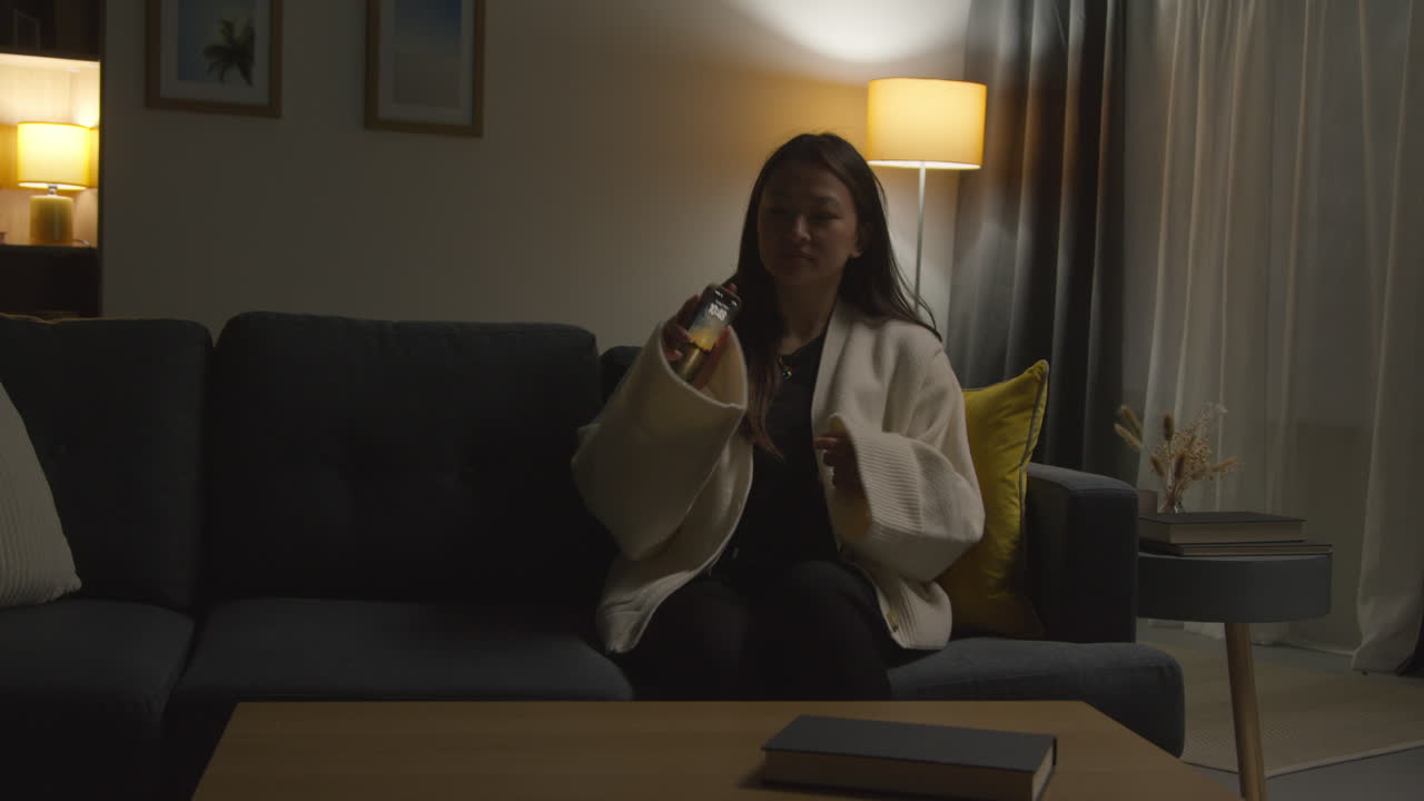 집에서 저녁을 보내고 소파에 앉아 휴대전화를 들고 인터넷이나 소셜 미디어를 스크롤하는 여성