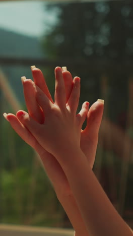 mom and daughter grasp hands in early morning light. relatives relax sitting on sunny glass balcony. caring mother looking after little child with intertwined fingers