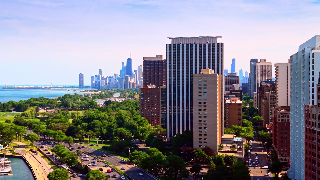 Torres altas com vista para a Lake Shore Drive, Chicago. O tráfego flui por uma rodovia à beira do lago, passando por áreas verdes e docas de marina, com o horizonte do centro da cidade ao longe