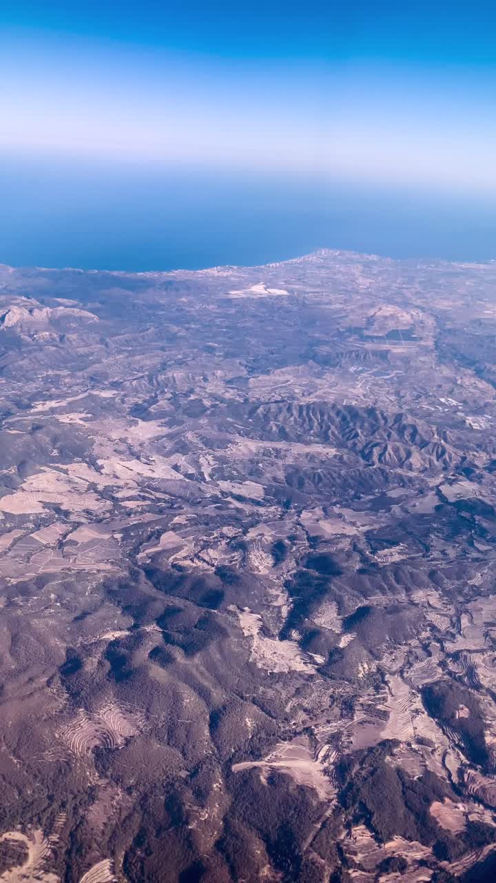 A foggy mountain landscape unfolds through the airplane window, shrouded in mist with no greenery in sight, creating an eerie yet captivating, otherworldly atmosphere.