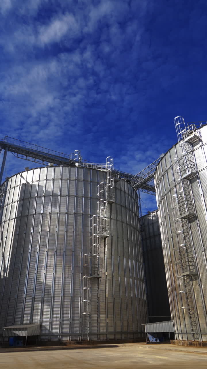 Huge granary outdoors. Large metal elevators on sky background. White smoke released into the air from industrial silos. Vertical video