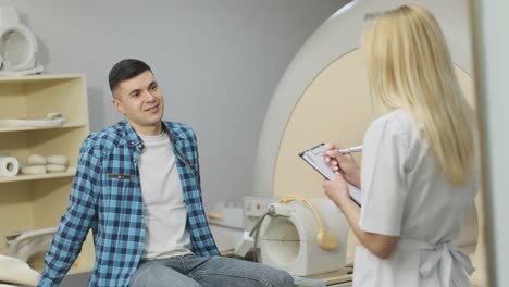 woman doctor radiologist has a dialogue with young male patient, asks and notes the patient's medical history, complaints in modern clinic beside modern closed-type mri