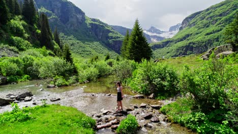 Woman-Hiking,-Crossing-River-Stream-in-Beautiful-Switzerland-Swiss-Alps-Mountains