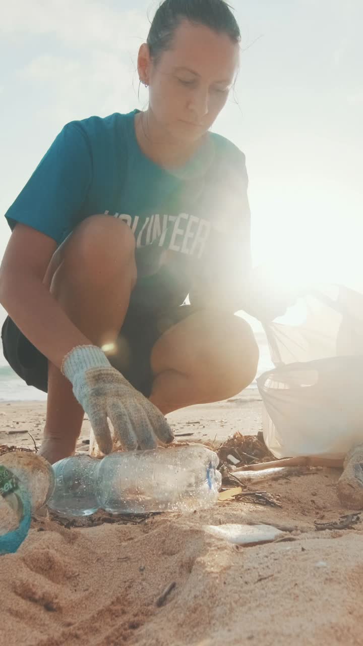 Young caring caucasian woman volunteer cleans beach of plastic bottles