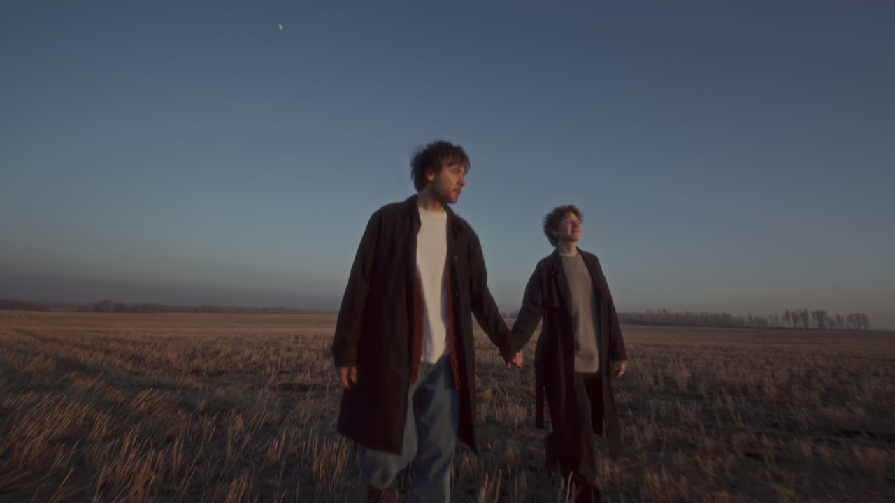 Couple Holding Hands and Walking through Open Field at Sunset