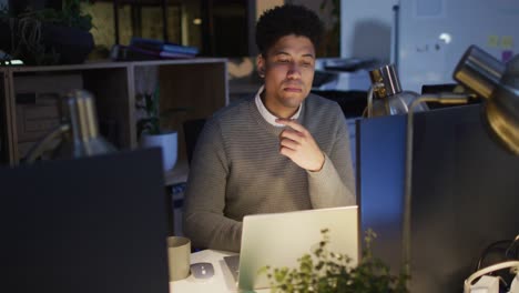 Video-De-Un-Hombre-Birracial-Enfocado-Usando-Una-Computadora-Portátil,-Trabajando-Hasta-Tarde-En-La-Oficina