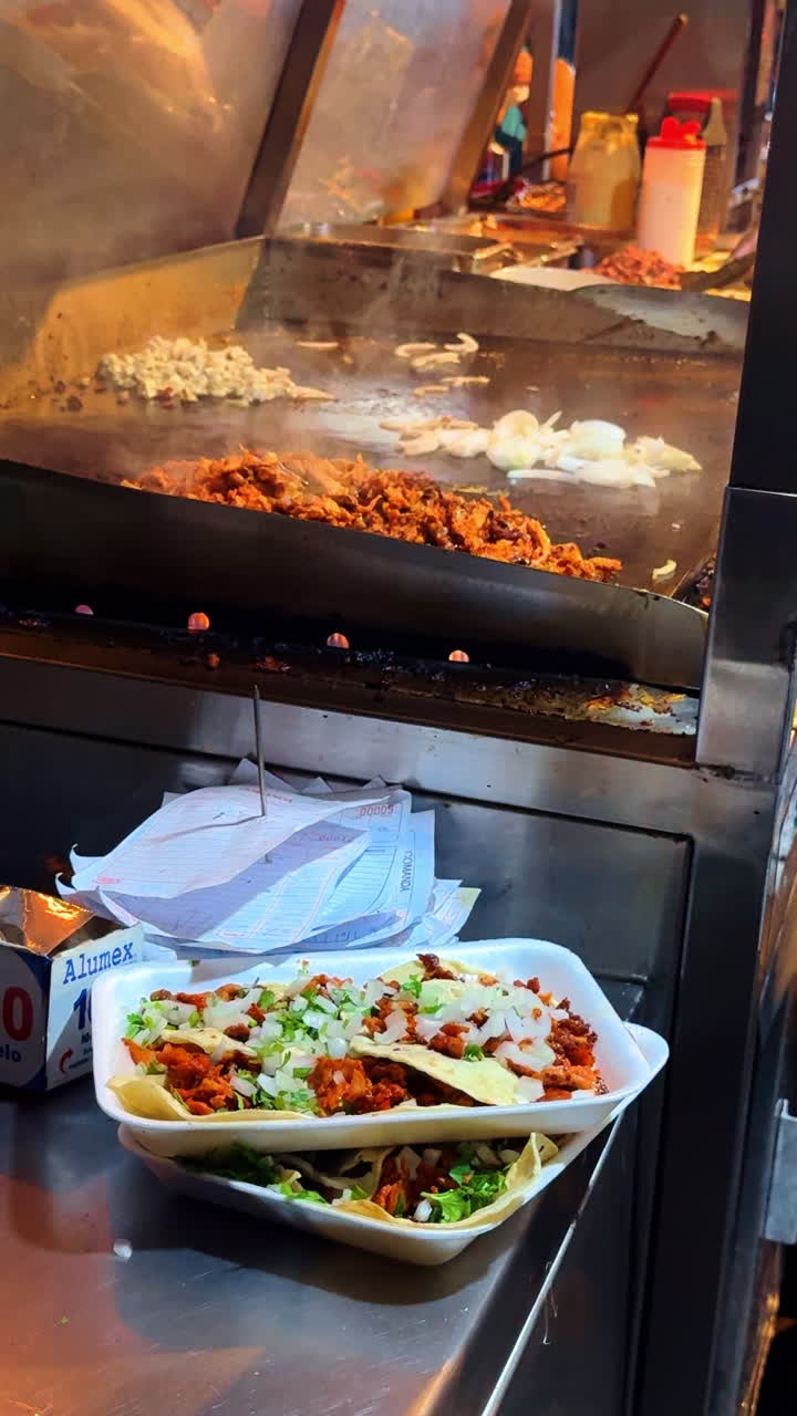 Tulum, Mexico, 5 August 2025: Street food vendor preparing tacos on a flat metal griddle. Close up of meat and onions cooking on a commercial griddle with served tacos