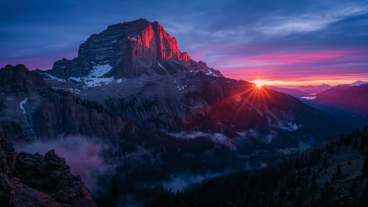 Sole nascente sulla cresta nella valle alpina che illumina il massiccio montuoso frastagliato con un caldo alpenglow e nebbia