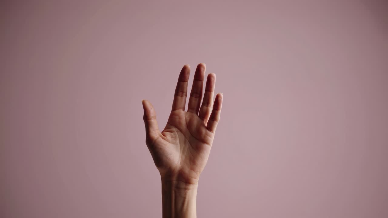 Das Video zeigt ein minimalistisches Konzept, das sich auf eine einzelne Hand vor einem sanften Rosa konzentriert.