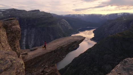 hiker with dog stands on trolltunga cliff in norway at sunset, feeling awe and peace, trolltunga