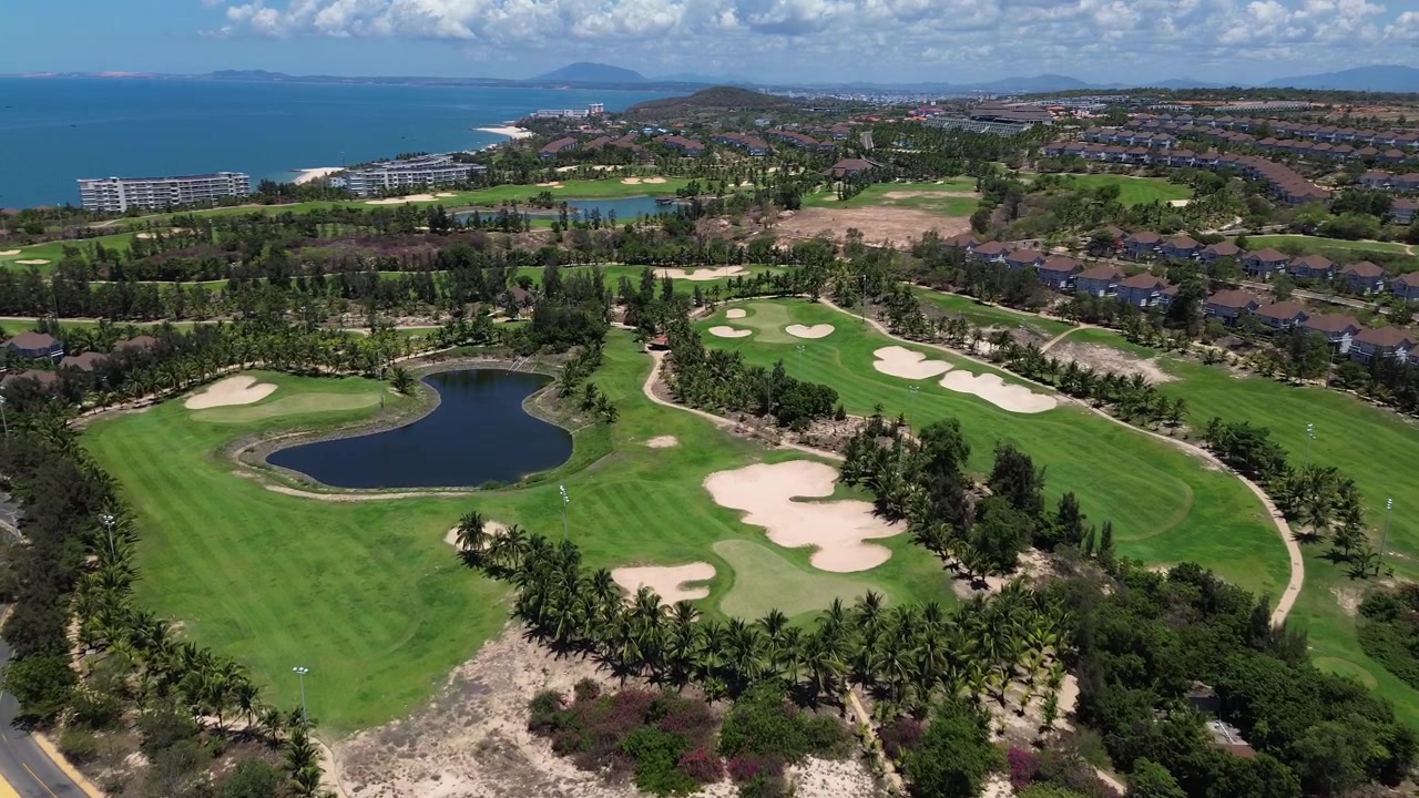 Riprese aeree con drone di un campo da golf panoramico a Mui Ne, Phan Thiet, Vietnam, che mostrano fairway e green curati circondati da vegetazione tropicale e un bellissimo paesaggio costiero nel Sud-est asiatico