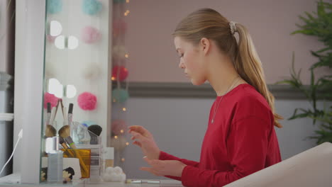 Teenage-girl-looking-in-mirror-in-bedroom-at-home-taking-off-make-up-and-moisturizing-skin---shot-in-slow-motion