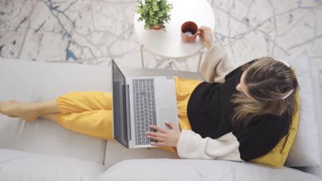 relaxed girl lying on the sofa works on the laptop.