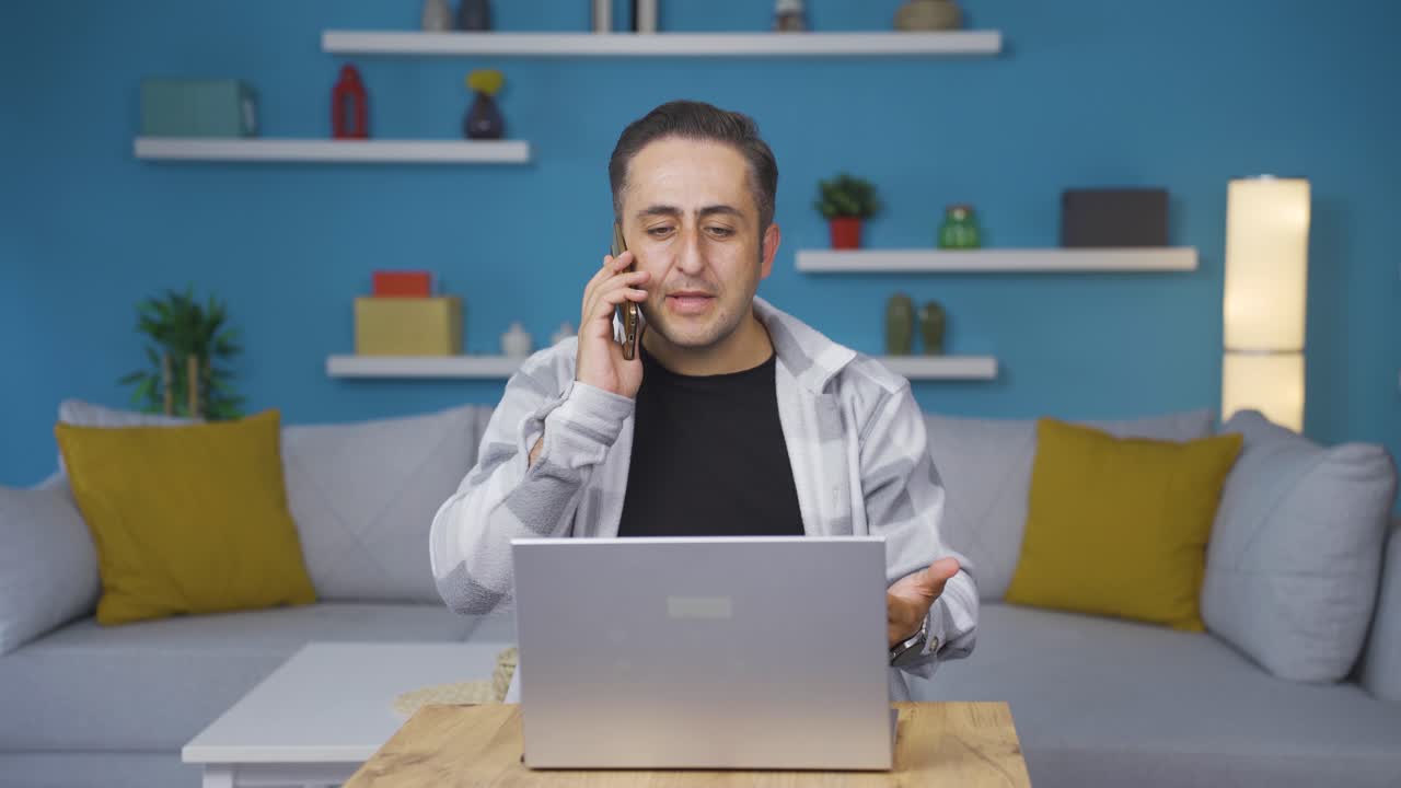 hombre usando una computadora portátil hablando nerviosamente por teléfono.