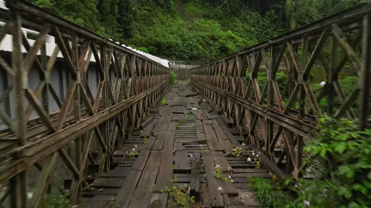 Aerial view of a rusted truss bridge with broken wooden planks and overgrown vegetation, nestled in a lush Philippine forest, evoking history and nature’s quiet reclamation