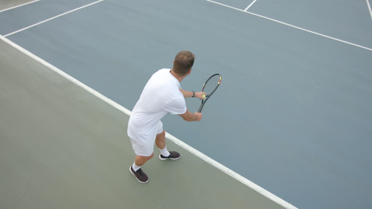 코카시안 남성 테니스 선수가 야외 테니스 코트에서 느린 동작으로 공을 기 위해 준비하고 있습니다.