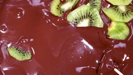 kiwi slices being dipped in melted chocolate