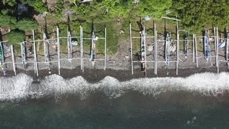 Jukung-fishing-boats-at-Amed-beach-Bali-Indonesia-with-soft-waves-hitting-the-shoreline,-Aerial-top-view-pan-right-shot