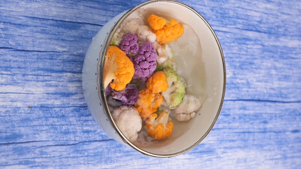 Fiori colorati di cavolfiore immersi nell'acqua in uno scolapasta