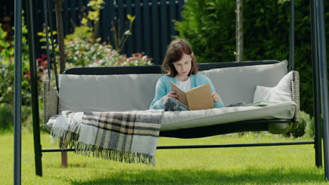 child reading a book, sitting in a garden swing in the backyard of a house