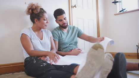 couple sitting on floor looking at floor plans in empty room of new home