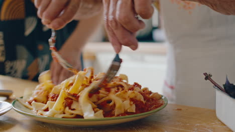 hands mixing freshly cooked pasta with tomato sauce on plate