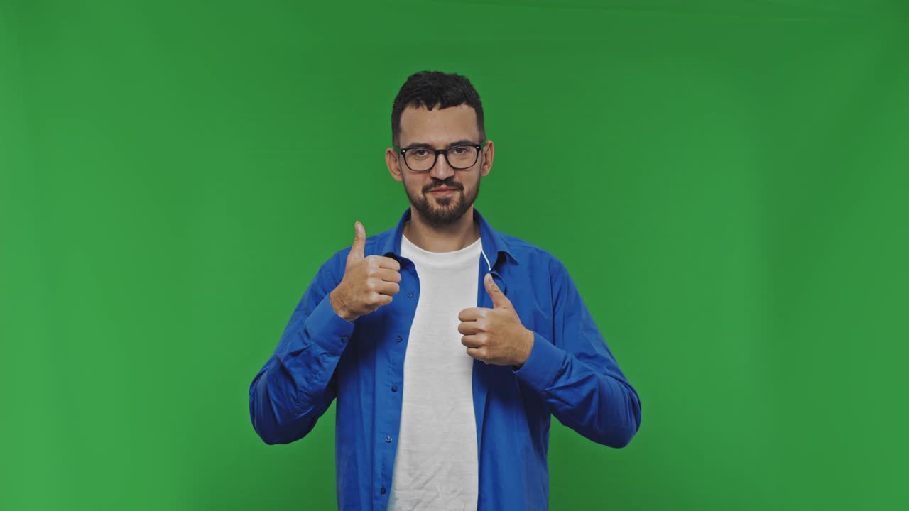 retrato de un joven sonriente mostrando un gesto de dos pulgares hacia arriba. tipo barbudo en el estudio en una pantalla verde.