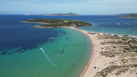 windsurfista che naviga lungo la spiaggia sabbiosa verso l'isola della penisola a porto pollo, sardegna - piedistallo aereo 4k su