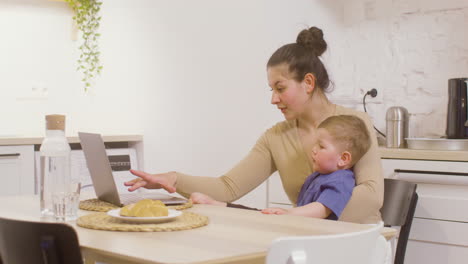 Junge-Mutter,-Die-Mit-Laptop-Computer-Arbeitet,-Während-Sie-Ihren-Kleinen-Jungen-Zu-Hause-Hält